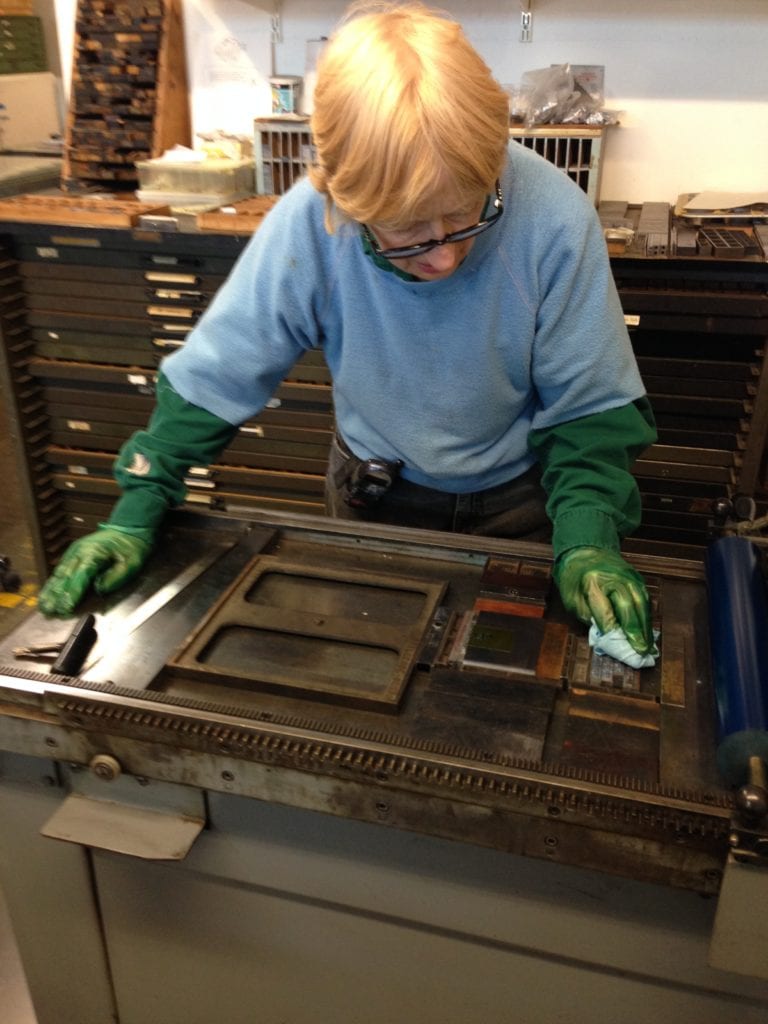 Mary cleaning the type, after her printing run is completed. 