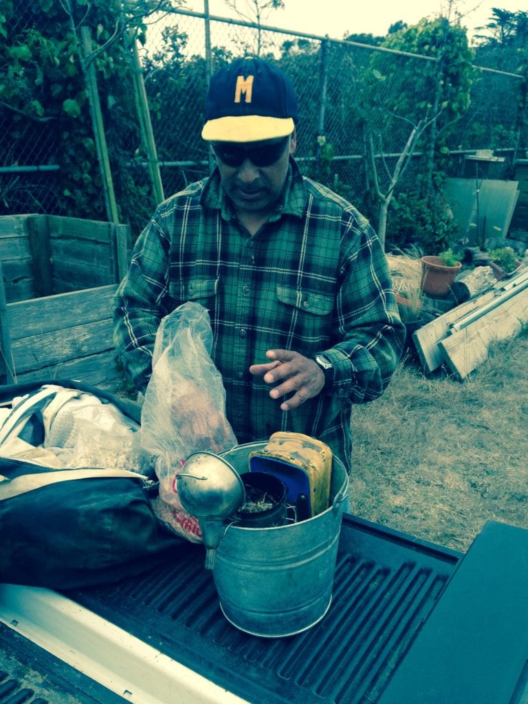 Fernado Aguilar, wearing his McAteer High School baseball cap, preparing to stoke his smoker, which he uses to calm his bees.